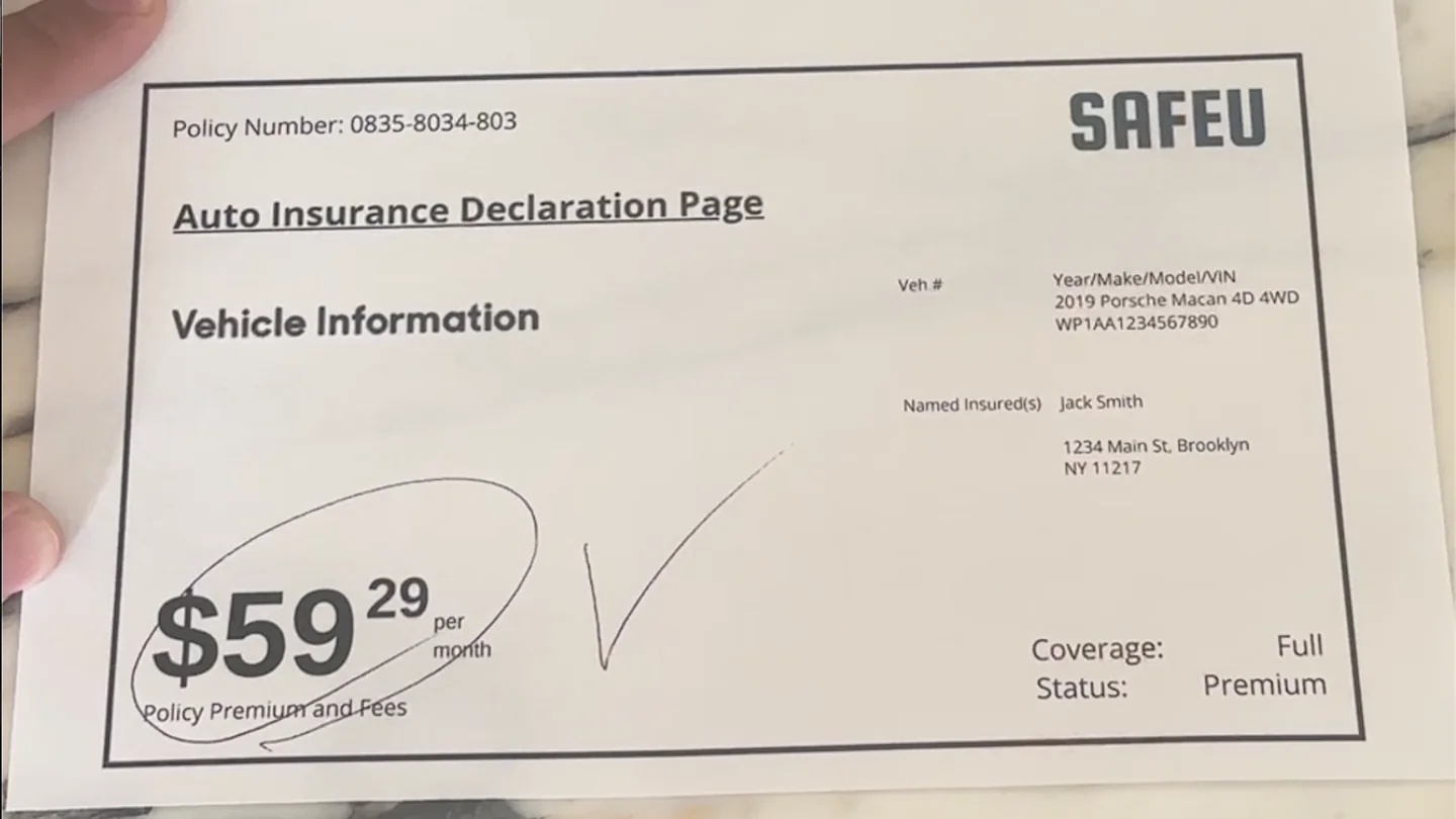 A hand holding an auto insurance declaration page on a kitchen counter, with the policy premium of $59.29 per month circled in pen and full coverage listed.